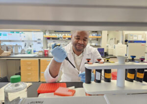 Jonas A. Kengne Ouafo, PhD, wearing laboratory PPE while pipetting reagents into a microcentrifuge vial.