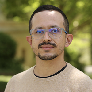 Headshot of Sebastian Duran, PhD, with a yellow building and plants in the background