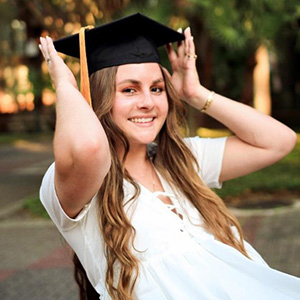 Picture of Alaina Keith putting on a graduation hat with the UF campus on the background